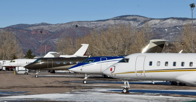 Several private jets parked on tarmac with mountains behind